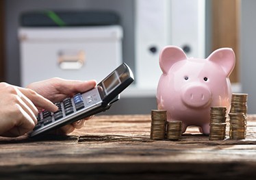 Man using a calculator at his desk with piggy bank and coin stacks nearby