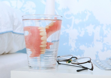 Closeup of denture in glass of water on bedside table