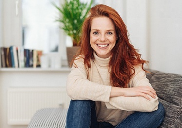 Red-haired woman sitting on couch with dental implants in Garland, TX