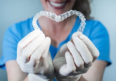 dental hygienist holding two Invisalign trays in the shape of a heart 