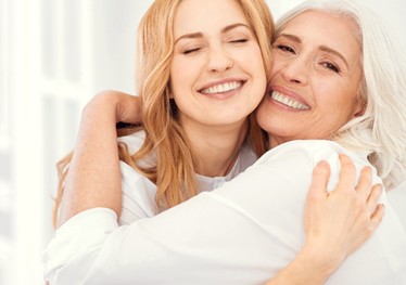 A young woman hugging an older woman and both smiling