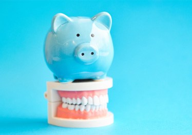 Model teeth and piggy bank representing cost of teeth whitening in Garland 